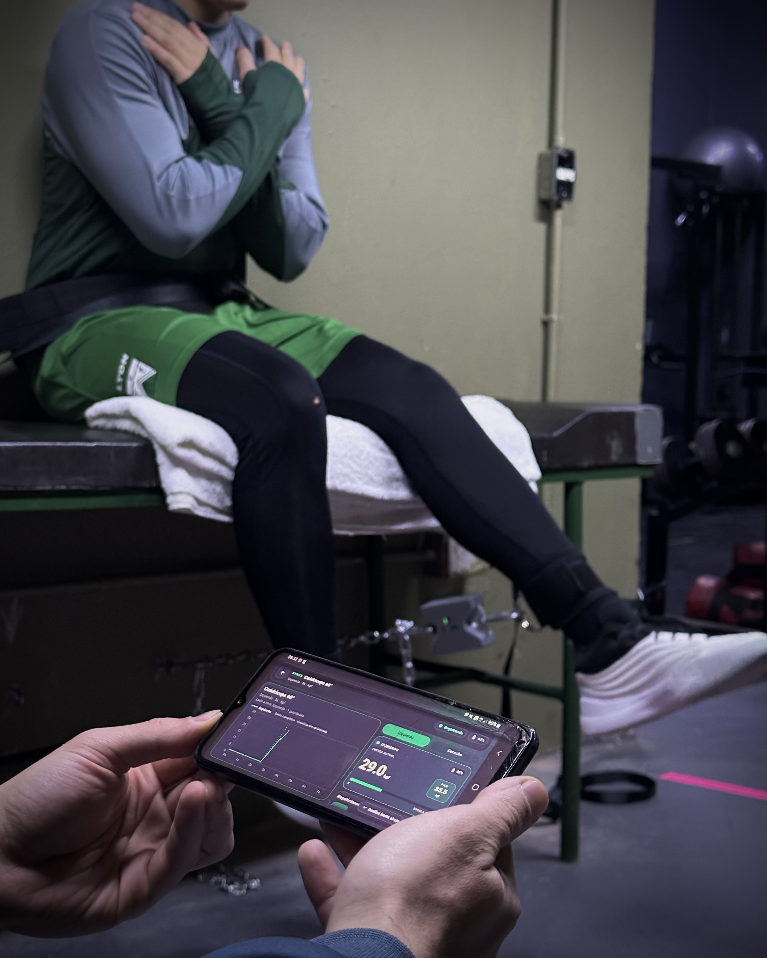 Evaluación isométrica con DYNEX: el profesional observa la curva de fuerza en el celular mientras el deportista realiza el esfuerzo